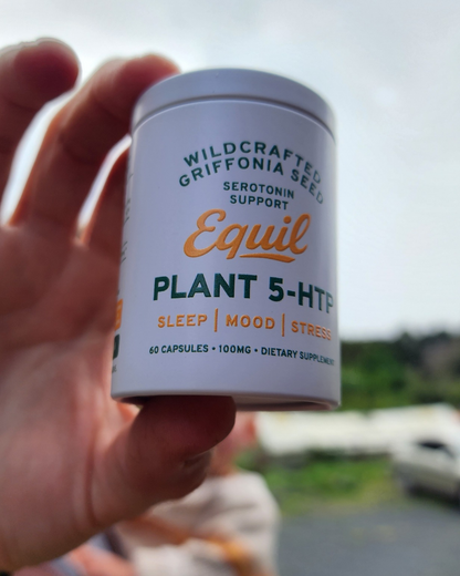 Hand holding a tub of Equil Plant 5-HTP capsules outdoors by the coast