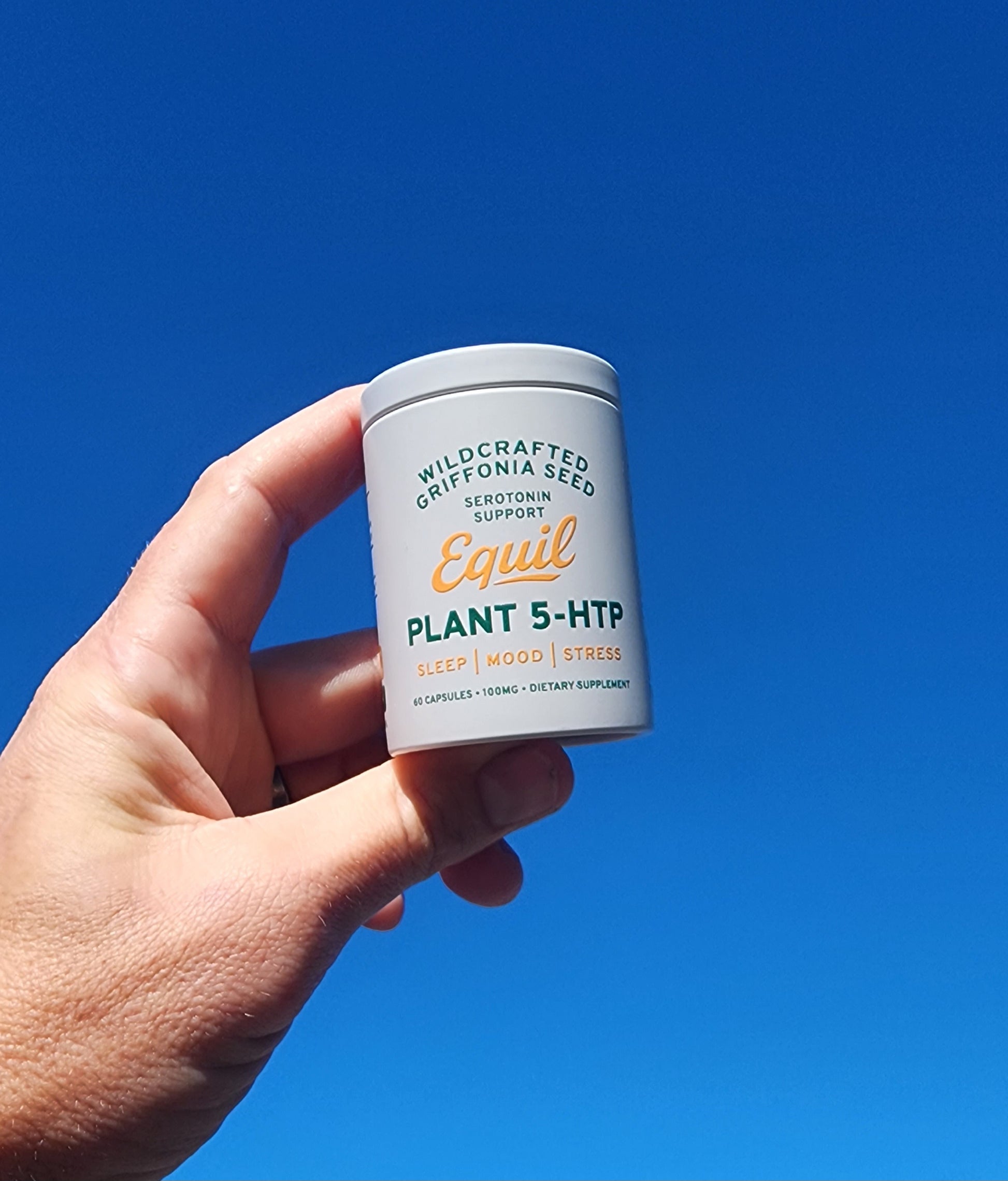 Hand holding a tub of Equil Plant 5-HTP capsules against a blue sky